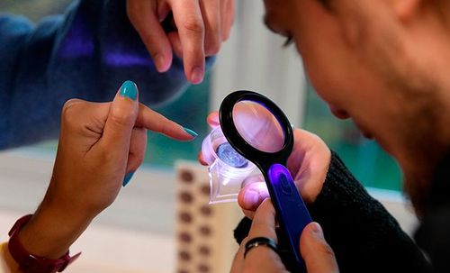 Fotografía del detalle de una lupa usada por una persona para mirar una moneda